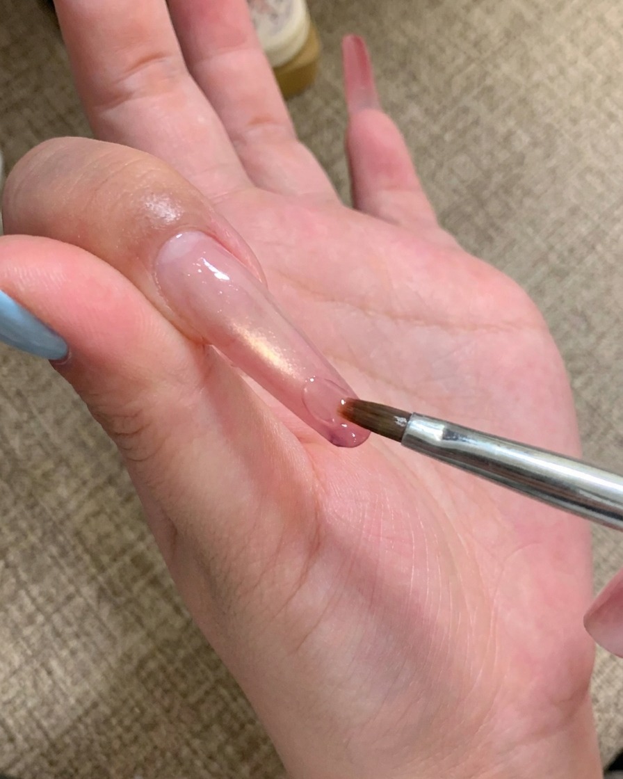 세밀한 브러시로 긴 손톱 끝에 투명 접착 젤을 바르는 모습.