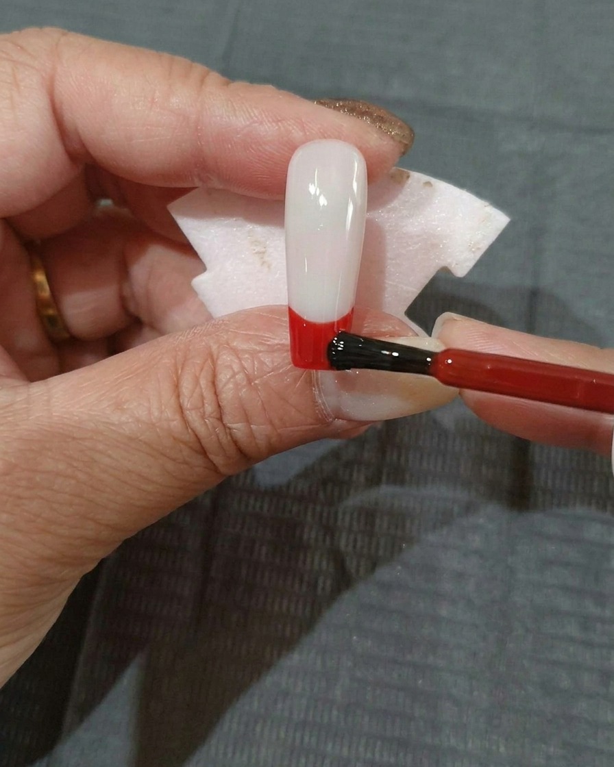 블랙 젤이 발린 손톱 아래쪽에 레드 젤 폴리시를 바르는 모습