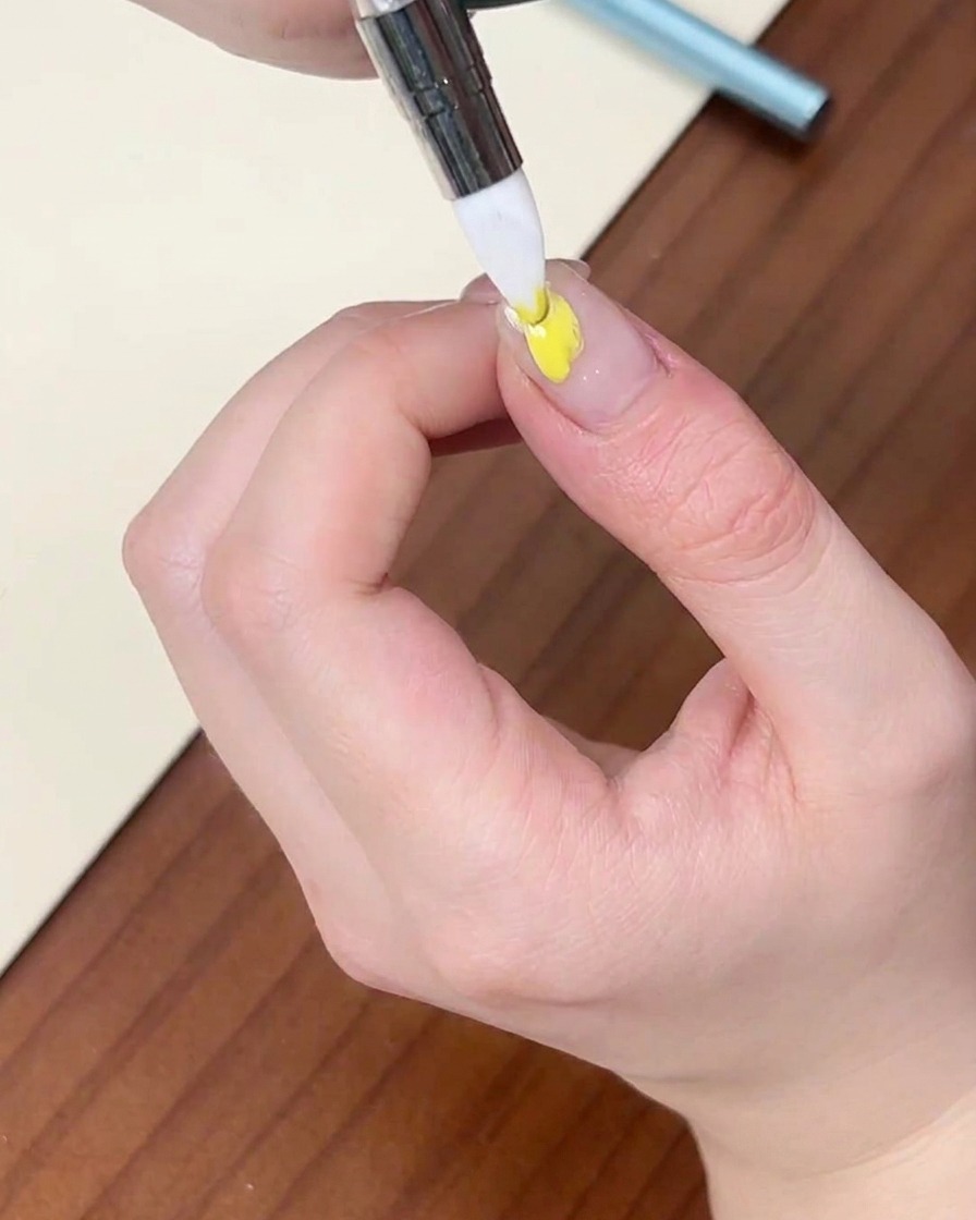 자연 네일 위에 얇은 라이너 브러시로 옐로우 컬러 젤 도트를 찍는 모습.