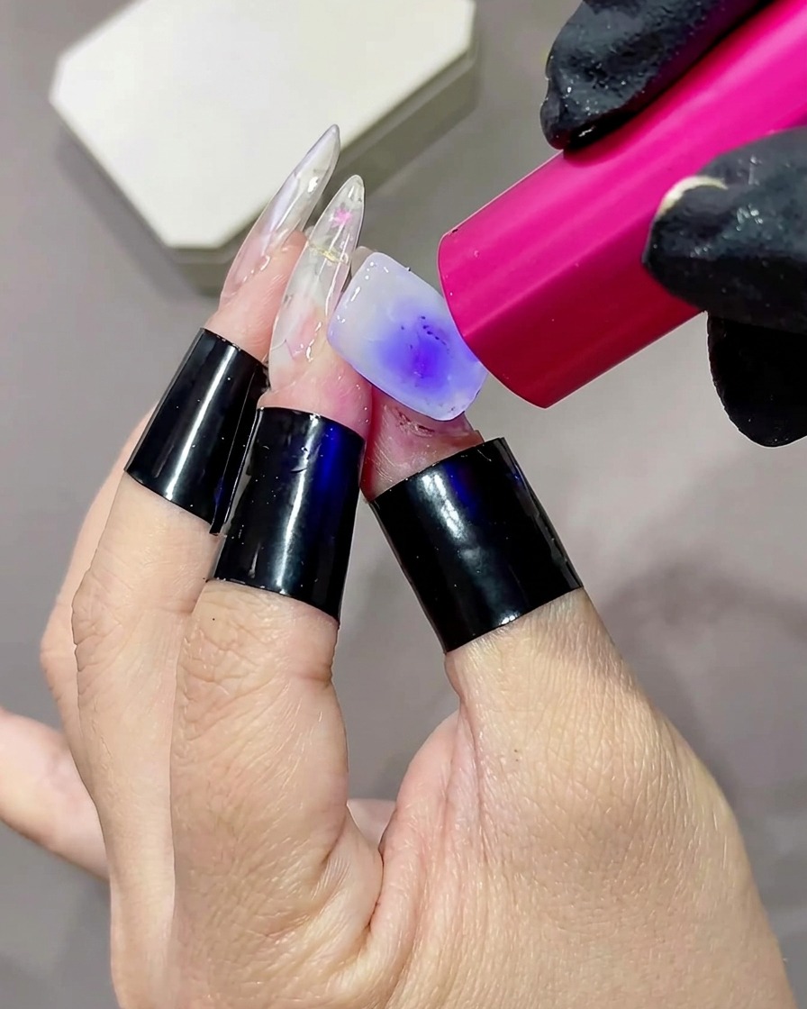 소형 핑크색 휴대용 UV/LED 램프로 밀크 화이트 베이스 코트를 큐어링하는 클로즈업.