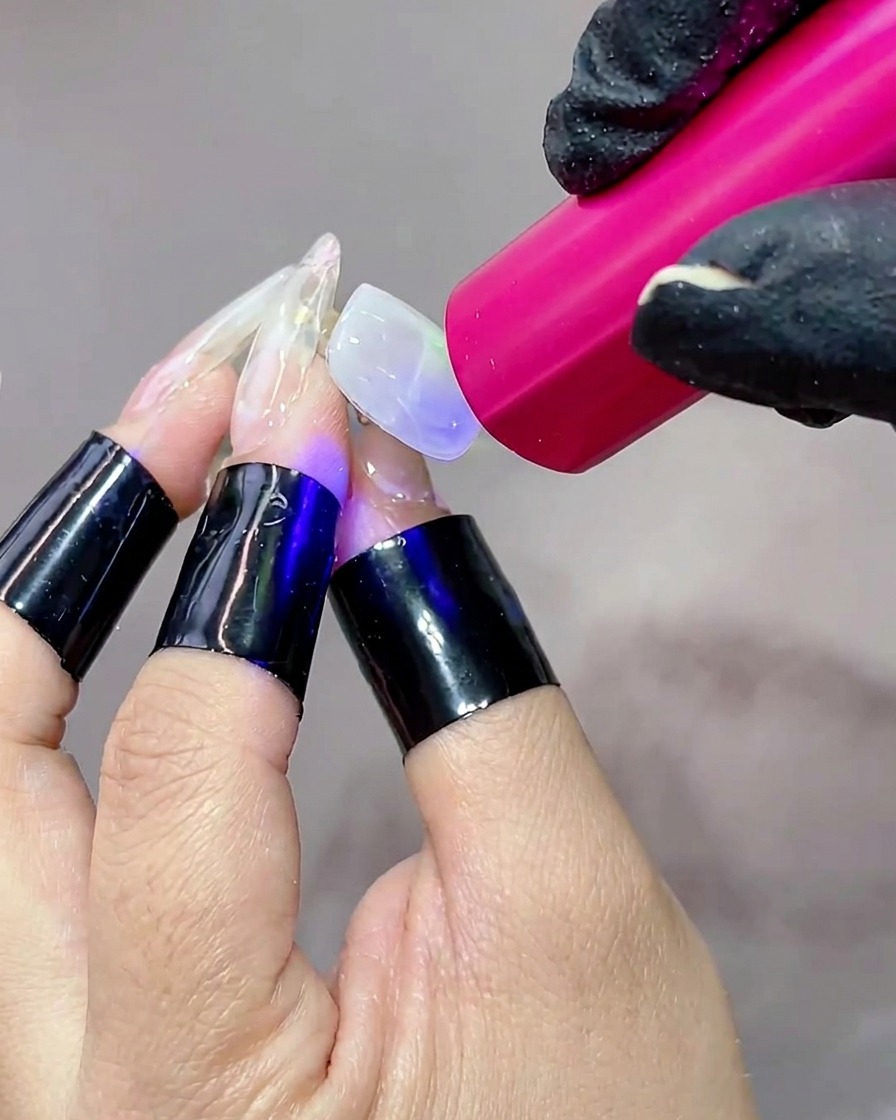 휴대용 UV 램프 아래에 손을 두고, 젤이 경화되며 네일 표면이 빛나는 모습.