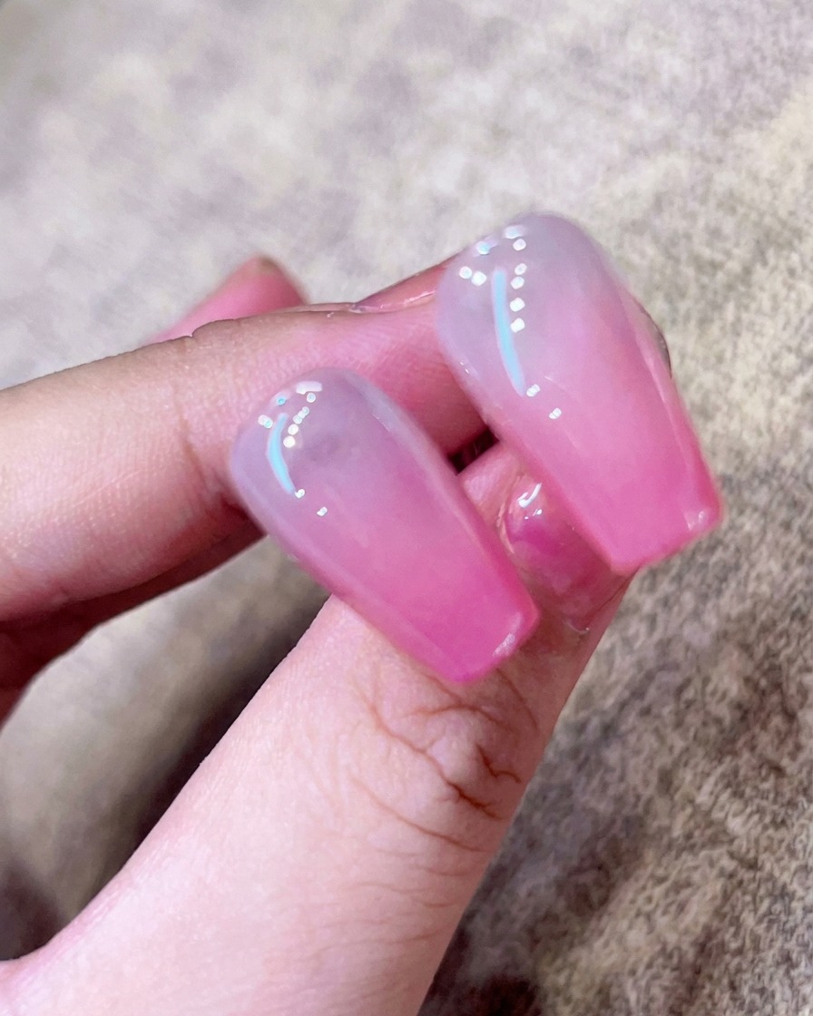 핑크 옴브레 네일 위에 브러시로 투명하고 윤기 나는 탑 코트를 바르는 클로즈업.