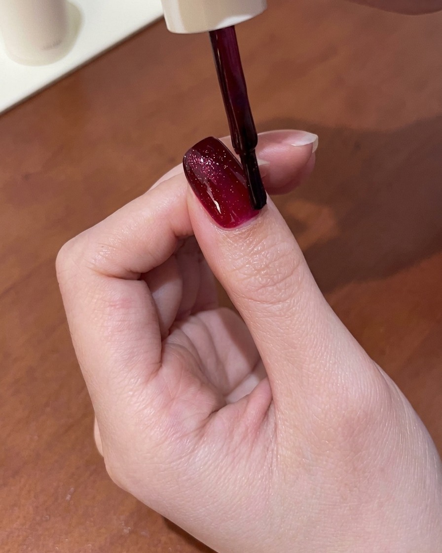 젖은 레드 캣아이 젤을 바른 손톱 위에 자석 도구를 가까이 대어 쉬머를 밝은 선으로 끌어당기는 모습.