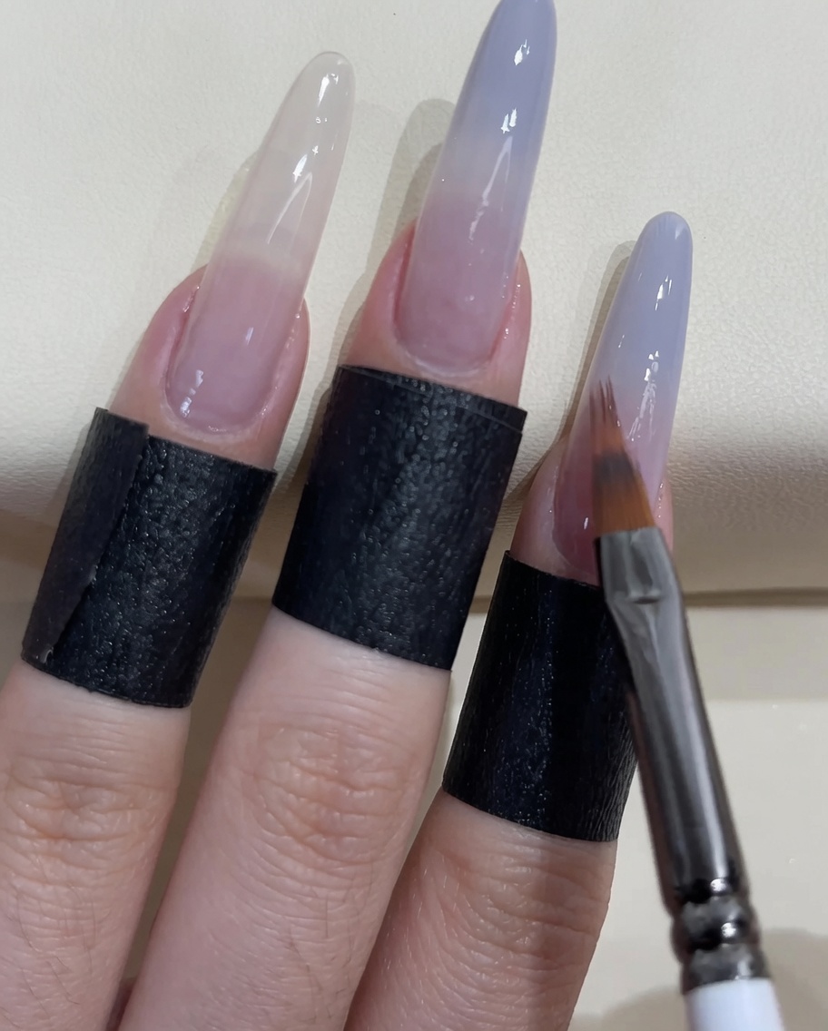 작은 네일 브러시로 손톱 끝부분에 그레이 블루 폴리시를 추가로 바르는 모습.
