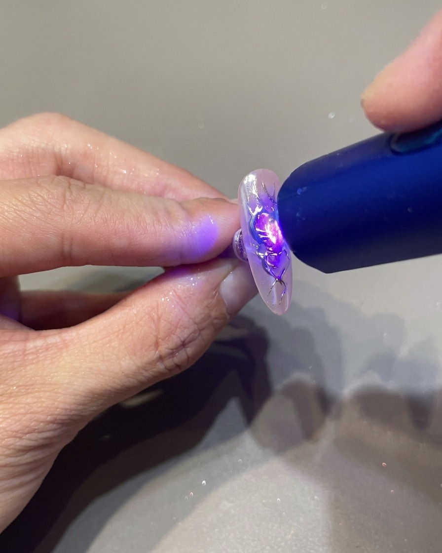 휴대용 UV 램프로 3D 젤 디테일이 올라간 손톱을 집중적으로 경화하는 모습.