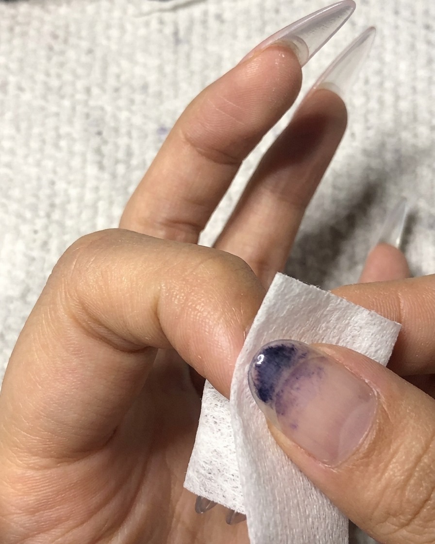 네일 클렌저가 묻은 보풀 없는 솜으로 약지 손톱 표면을 닦아내는 모습.