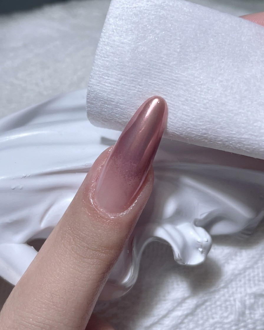 보풀 없는 패드를 사용하여 로즈골드 크롬 네일의 가장자리를 닦아내는 모습.