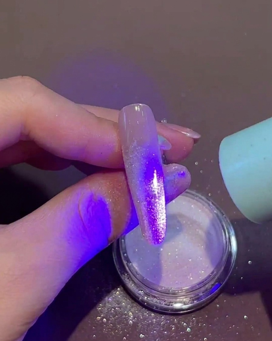 파우더가 뿌려진 젖은 젤 네일 위에 휴대용 UV/LED 램프를 직접 갖다 대고 큐어링하는 모습.