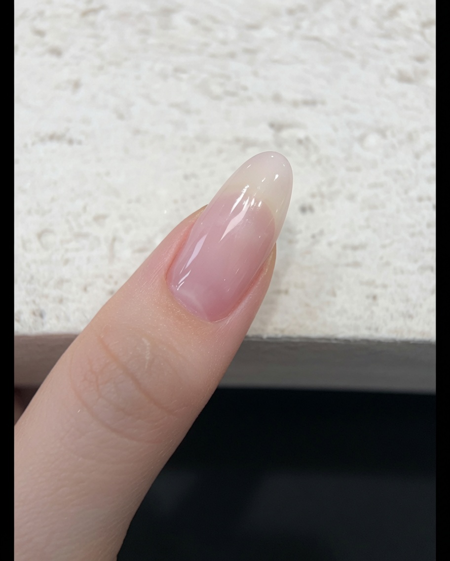 손톱에 투명한 누드 핑크 젤리 폴리시를 브러시로 얇게 펴 바르는 모습.