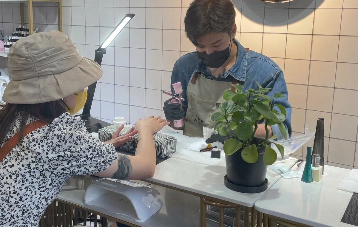 네일 아티스트가 에어브러시 도구를 잡고 흰 티슈에 분사 테스트를 하는 모습.