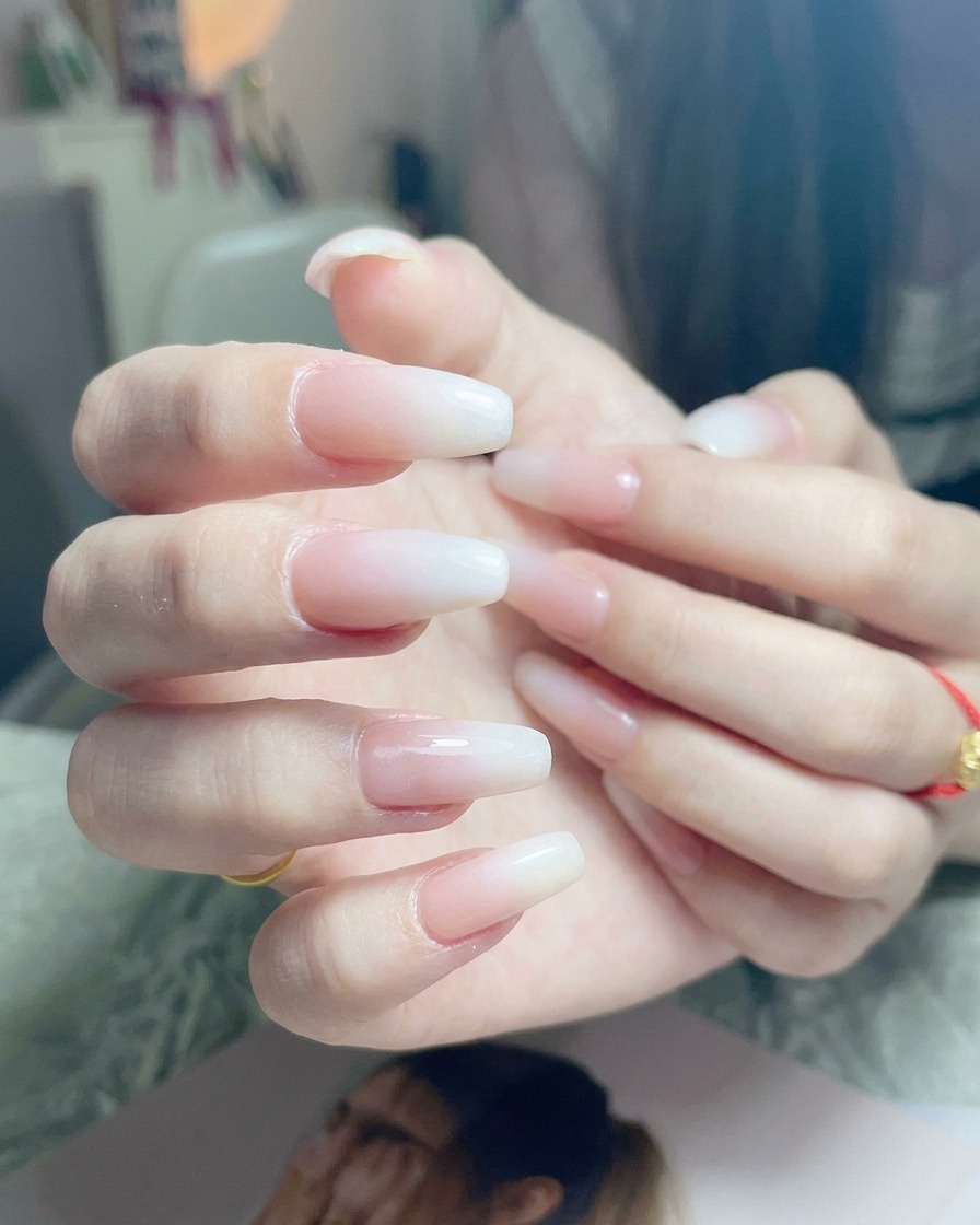 완성된 화이트 옴브레 네일 위에 투명한 글로시 탑 코트를 바르는 모습.