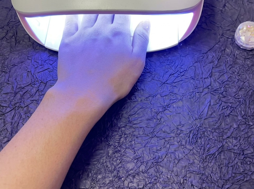 보라색 배경 위 UV/LED 램프 안에서 큐어링 중인 손