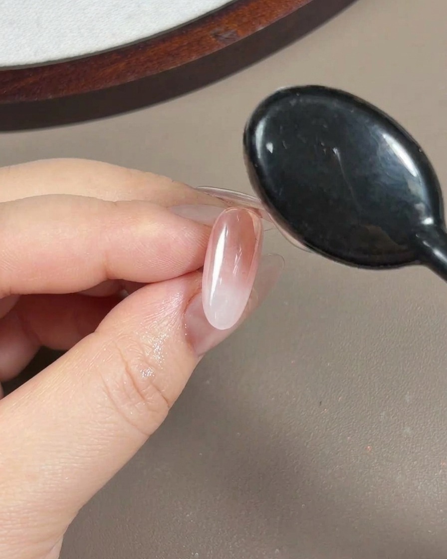 오로라 파우더가 발린 손톱 위에 점도 높은 투명 보강 젤을 브러시로 바르는 클로즈업 뷰.