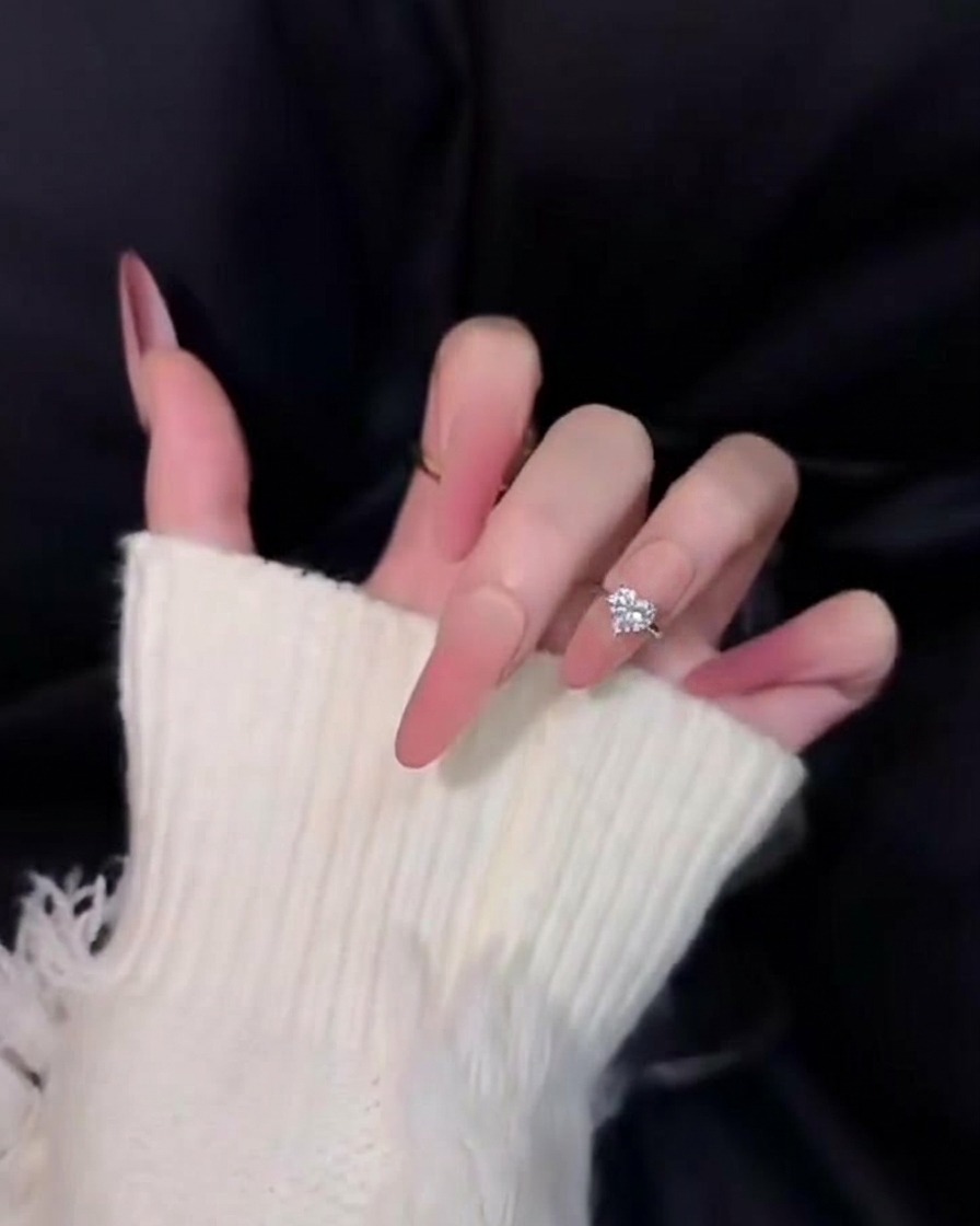 검은색 배경 위에서 벨벳처럼 부드럽고 매트한 느낌을 강조한 긴 핑크 옴브레 네일 근접 샷.