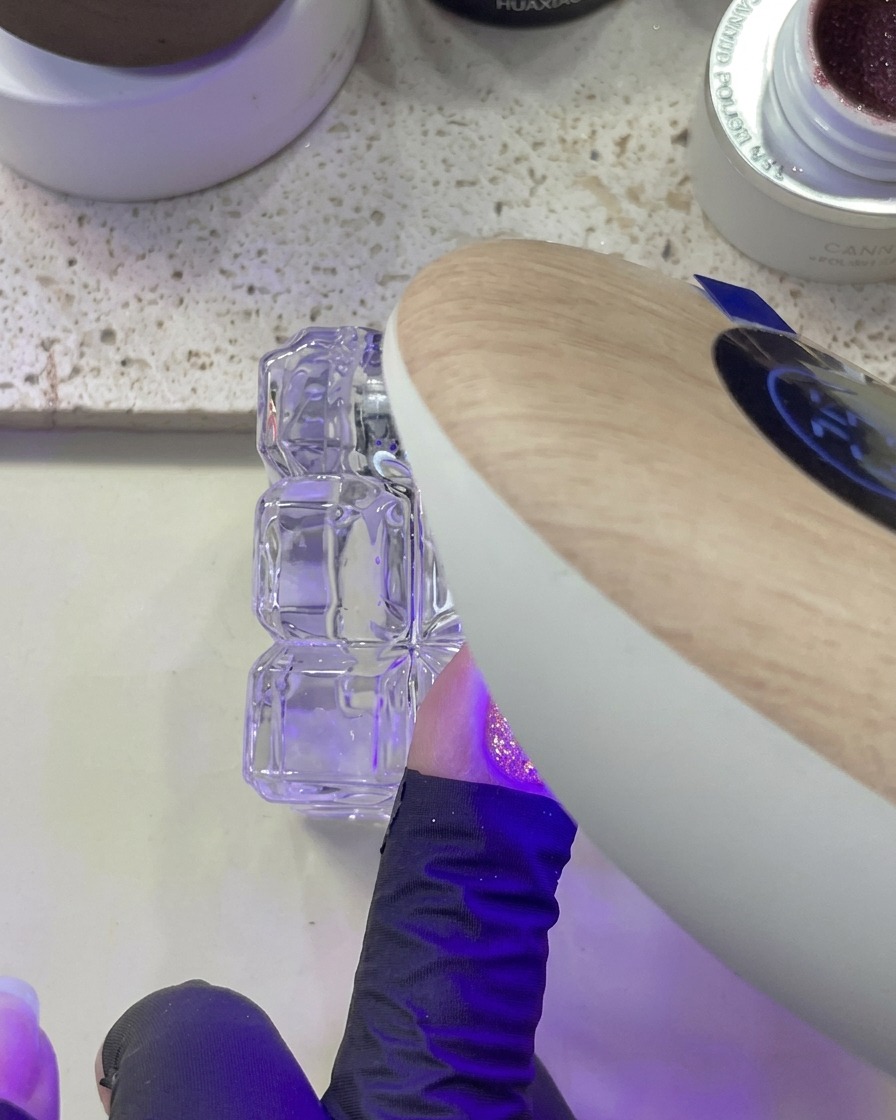 핑크 글리터가 발린 손톱을 UV/LED 램프에 넣어 큐어링하는 모습.