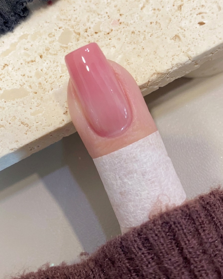 피치 옴브레 네일 위에 마지막으로 투명하고 광택 나는 탑코트를 바르는 모습.