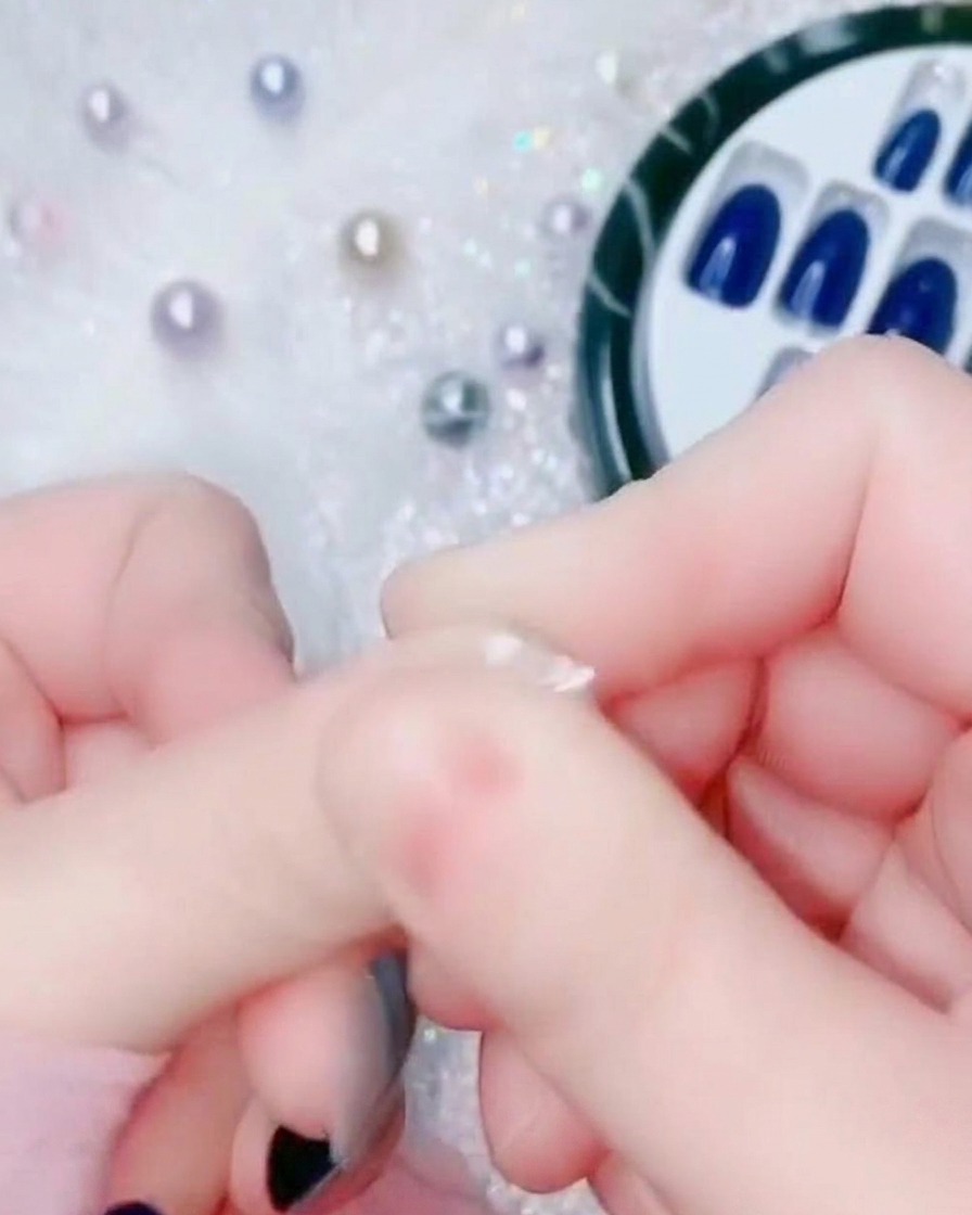 일렉트릭 블루 프레스온 네일의 밑부분을 자연 큐티클 영역에 대고 누르는 손가락 클로즈업.