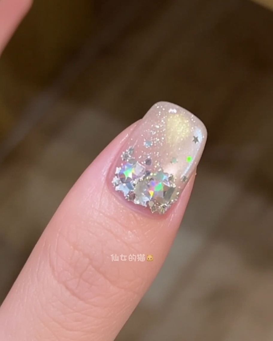 별 모양 스팽글로 장식된 손톱 위에 투명한 빌더 젤 층을 매끄럽게 펴 바르는 브러시 클로즈업.
