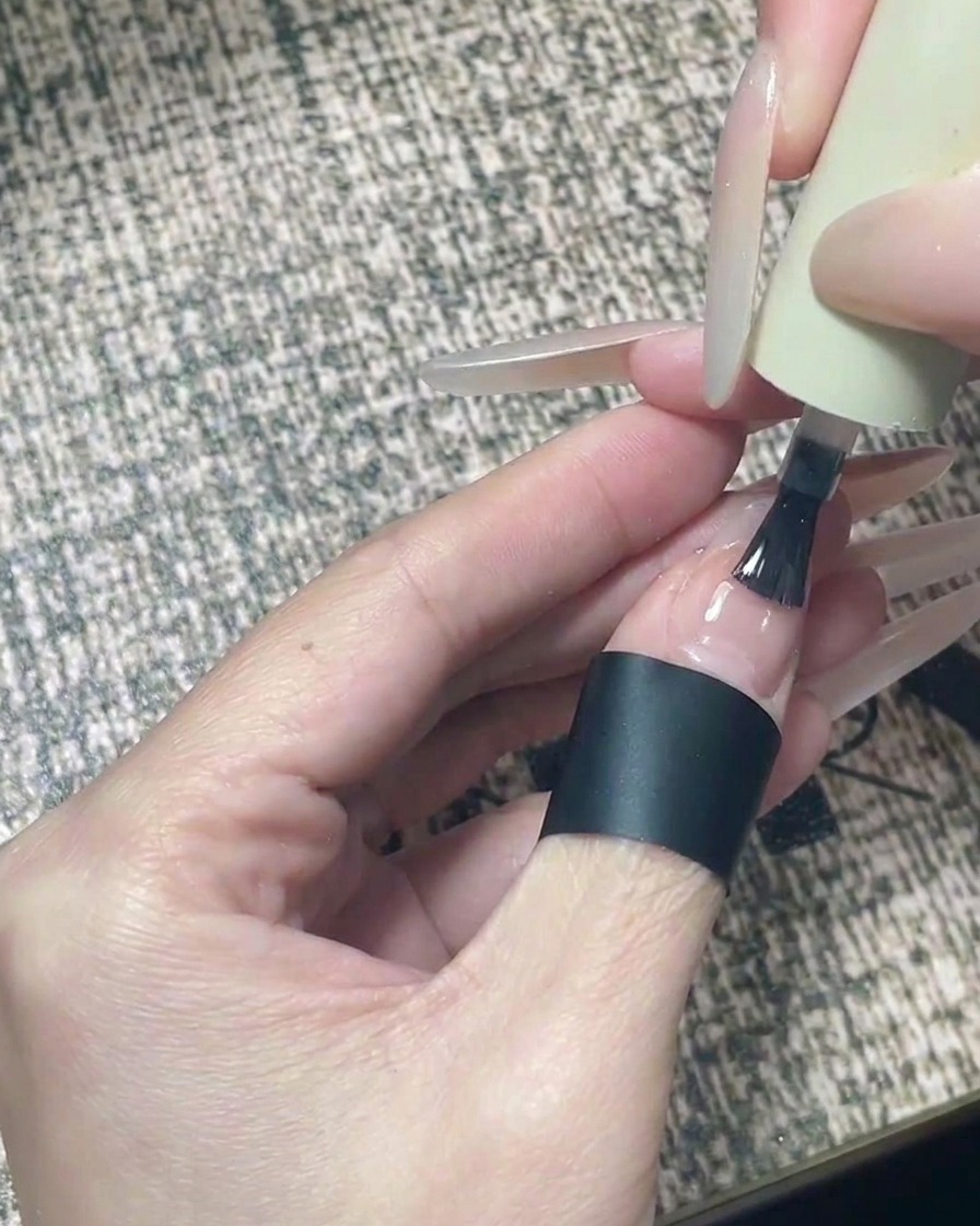 블랙 별 디자인이 완성된 손톱에 글로시 클리어 탑코트를 펴 바르는 모습.