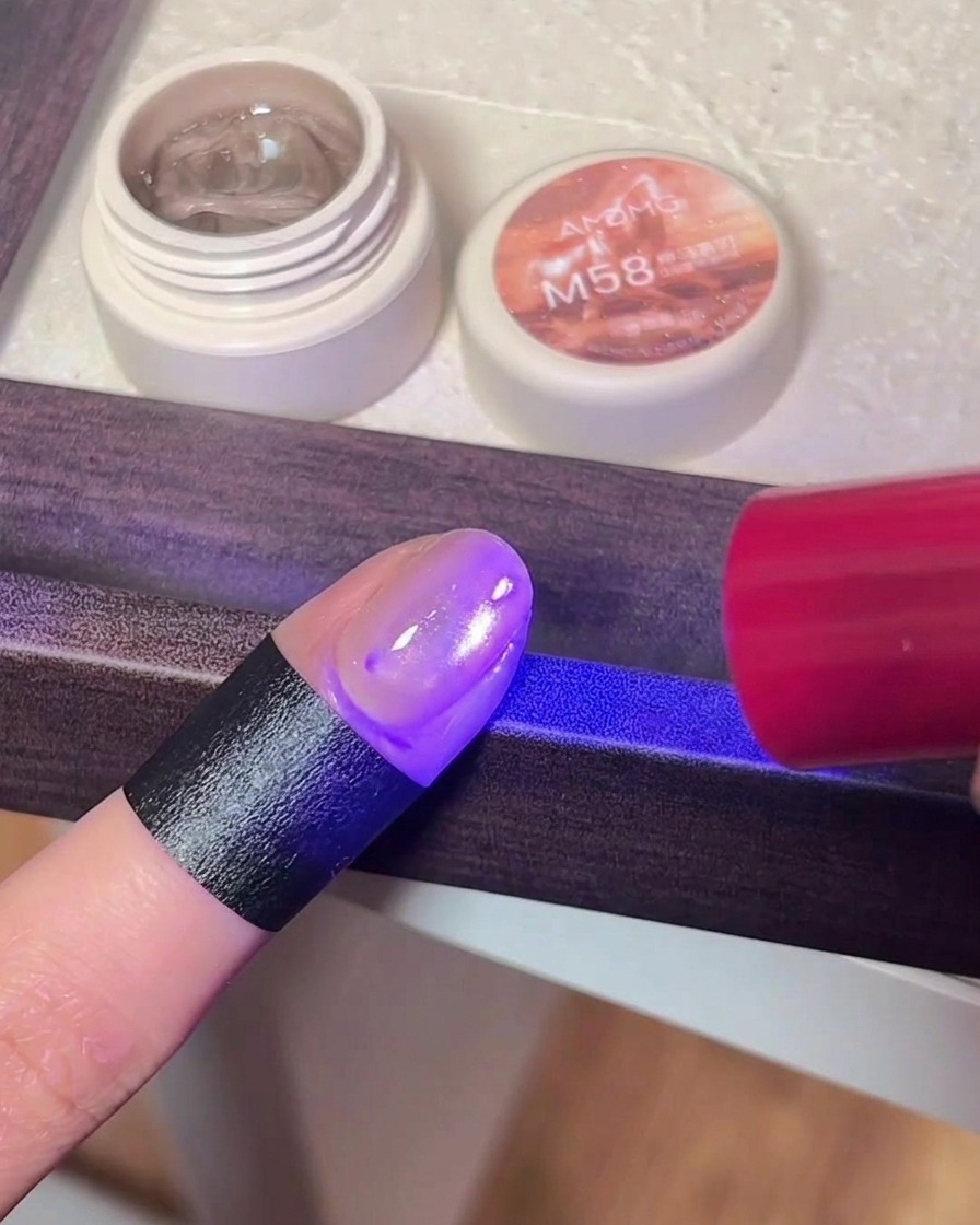 자석 젤 폴리시를 바른 손가락이 UV/LED 네일 램프의 보라색 불빛 아래 놓인 클로즈업 이미지.