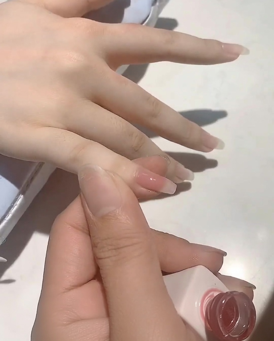 브러시로 손톱에 누드 핑크 젤 폴리쉬를 바르는 모습.