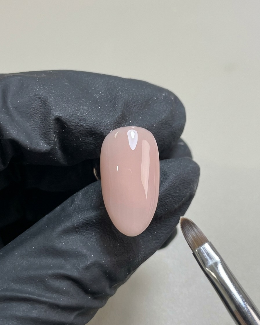 네일 아트 전, 매끄럽고 반투명한 누드 젤 베이스 코트를 바르고 큐어링을 마친 손톱 하나.