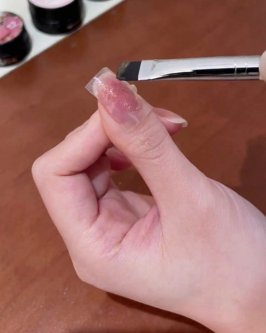 손톱에 붙인 나비 스티커 위에 골드 자석 젤을 브러시로 바르는 모습.