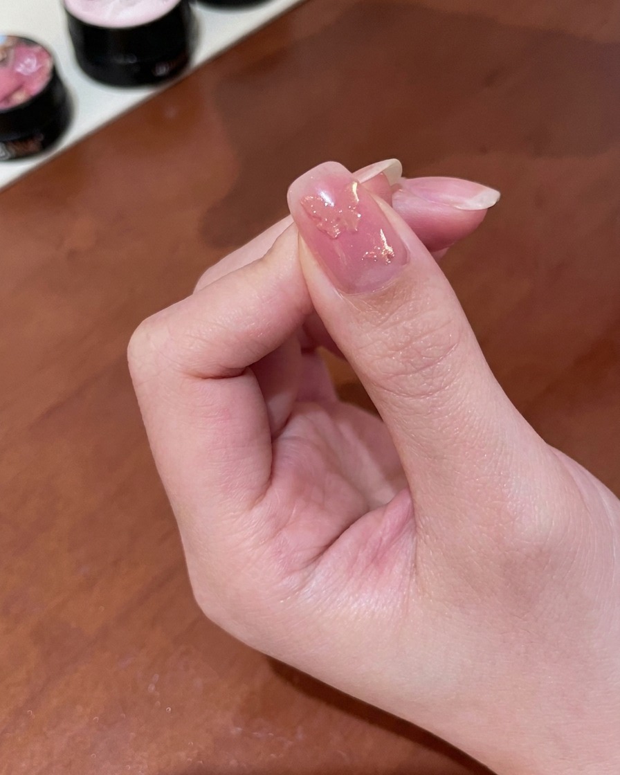 젖은 골드 자석 젤이 발라진 손톱 위로 작은 원기둥 모양의 자석을 들고 있어 오묘하게 빛이 변하는 펄을 연출하는 클로즈업 장면.