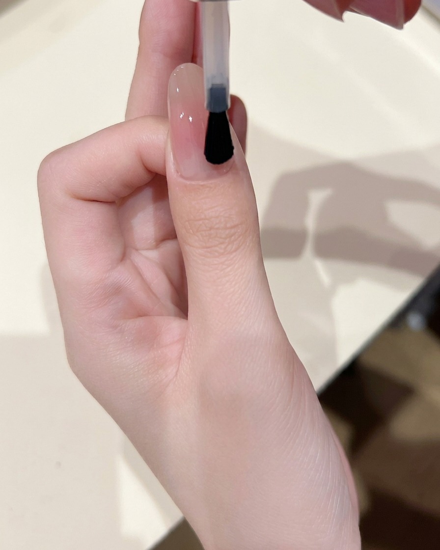 블러쉬 중심이 있는 손톱 위에 클리어 베이스 젤을 얇게 펴 바르는 모습.