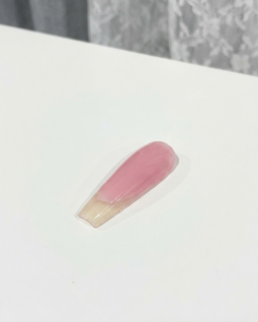 브러시를 사용해 손톱 위의 3D 핑크 리본 파츠 위로 탑 코트를 꼼꼼히 바르는 모습.
