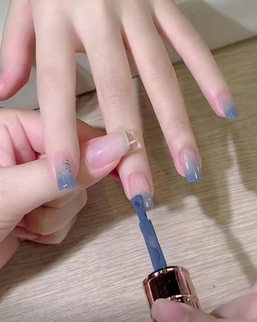 젤 폴리시 브러시로 정돈된 손톱 끝에 더스티 블루 컬러를 바르는 모습.