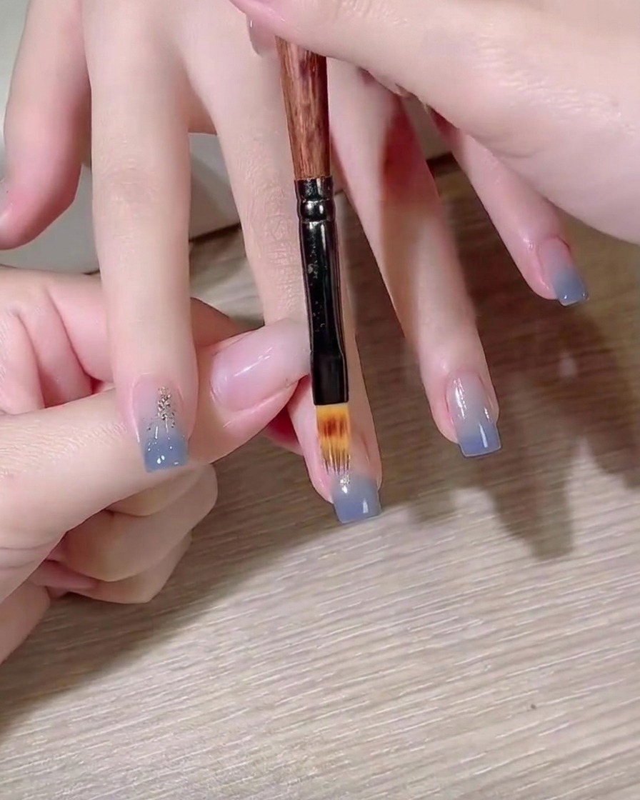 평붓을 사용하여 손톱 위에서 블루 컬러 그라데이션을 블렌딩하는 모습.