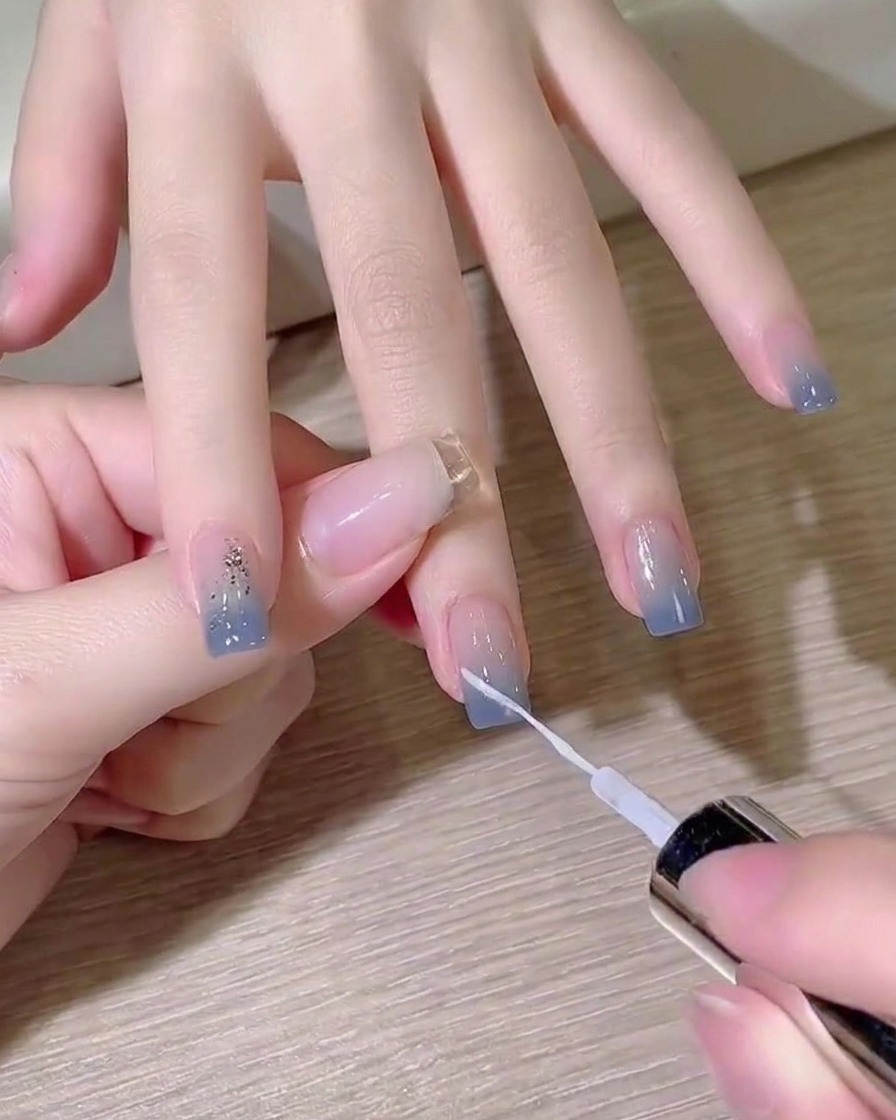 라이너 브러시로 블루 옴브레 네일 위에 선명한 화이트 대각선 라인을 그리는 모습.