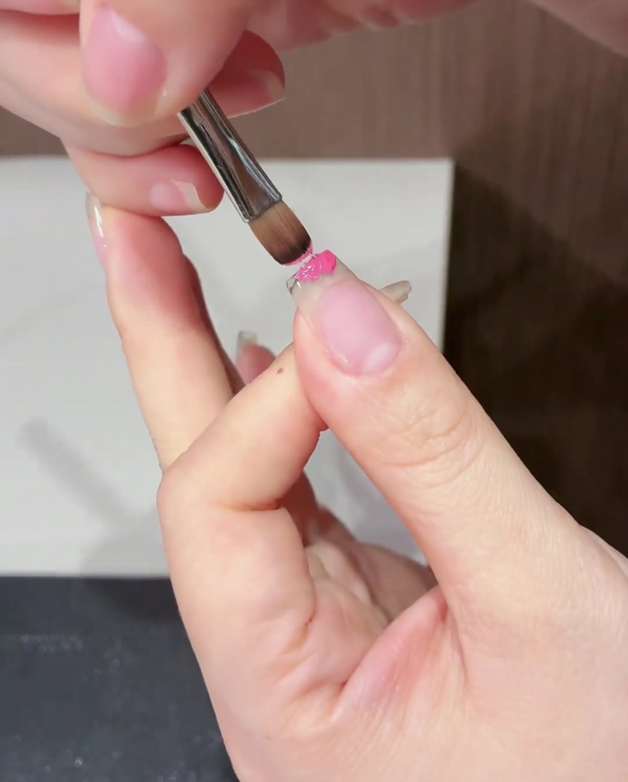 평붓을 사용하여 손톱 끝부분에만 마젠타 젤을 조심스럽게 바르는 모습.