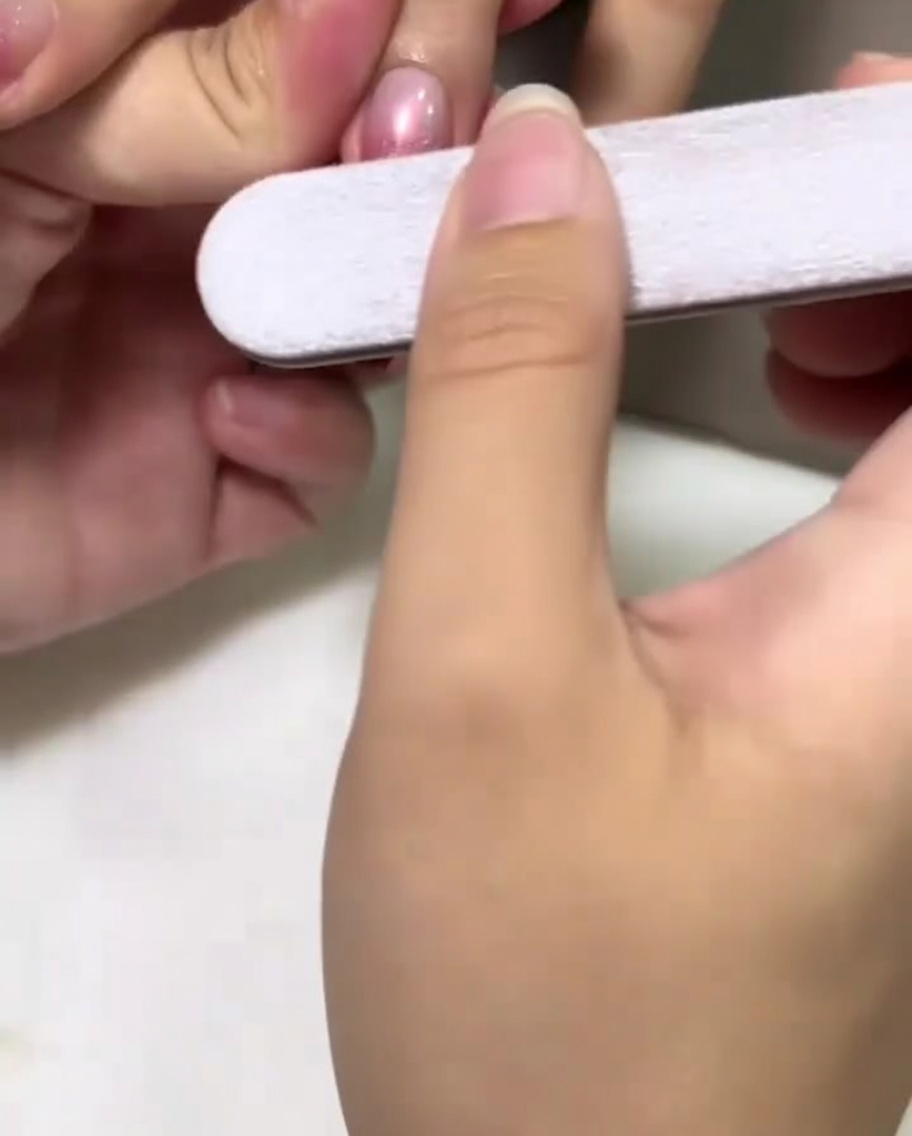 핑크색으로 컬러링된 네일 중앙을 네일 파일로 부드럽게 버핑하는 손.