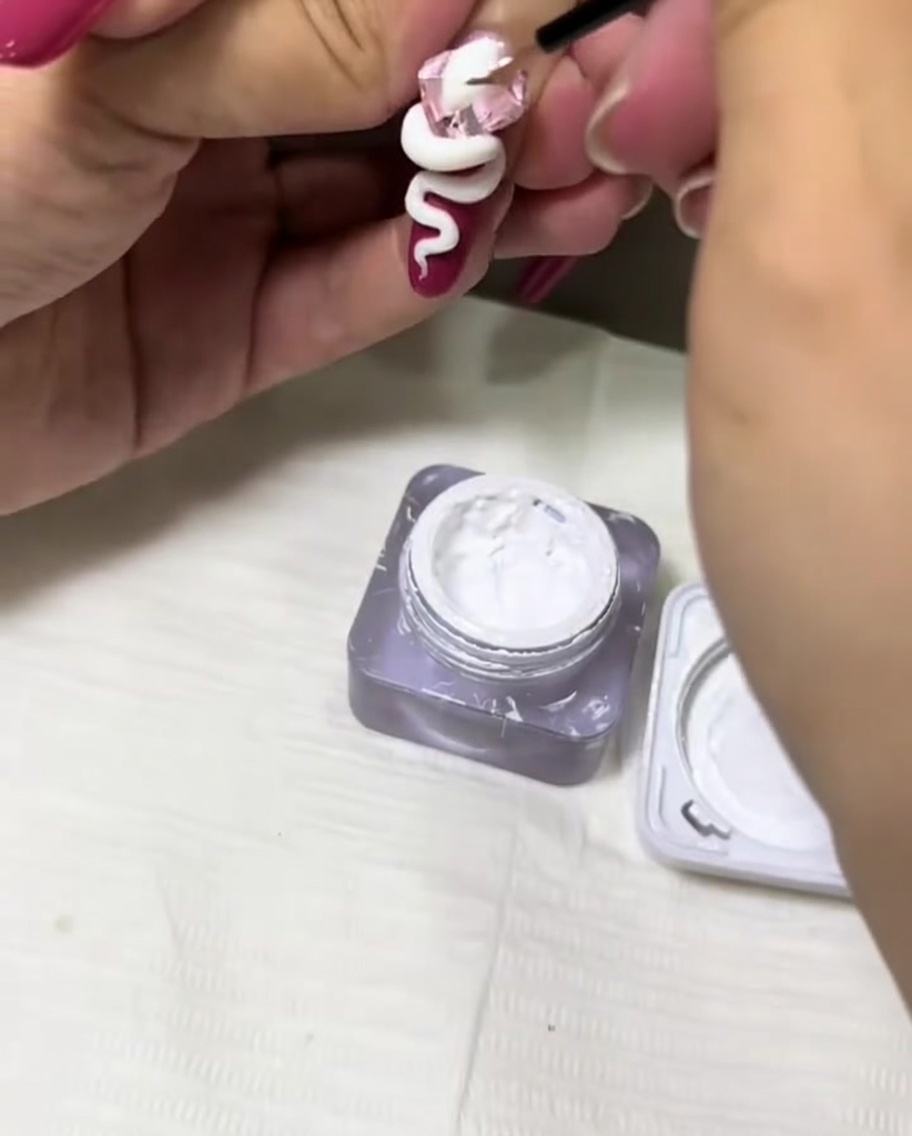 네일 위에 조각된 3D 뱀 디자인에 얇은 디테일 브러시로 화이트 젤을 발라 질감을 더하는 모습.