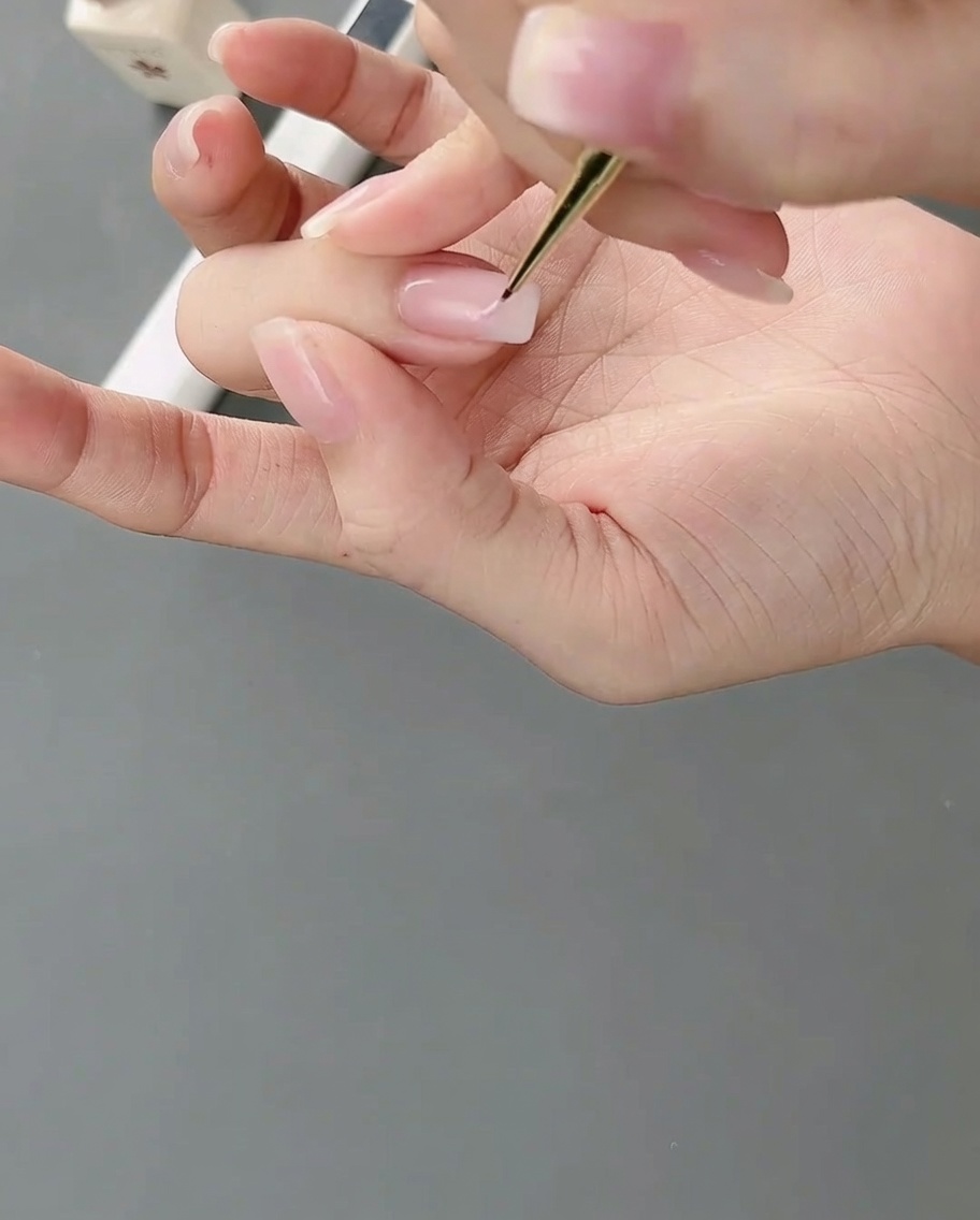 세밀한 네일 아트 브러시로 손톱 위에 연핑크 젤을 발라 불규칙한 컬러 블록을 그리는 모습.