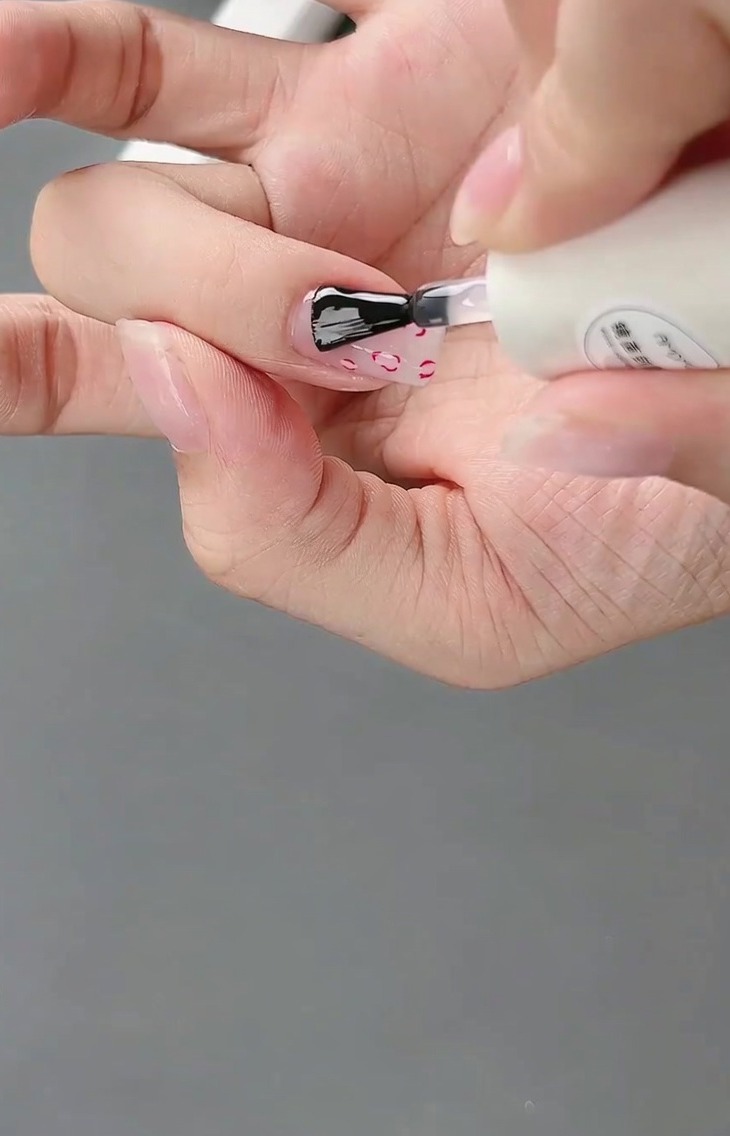 완성된 프렌치 및 3D 리본 네일 디자인 위에 마무리로 광택 있는 탑코트를 바르는 모습.