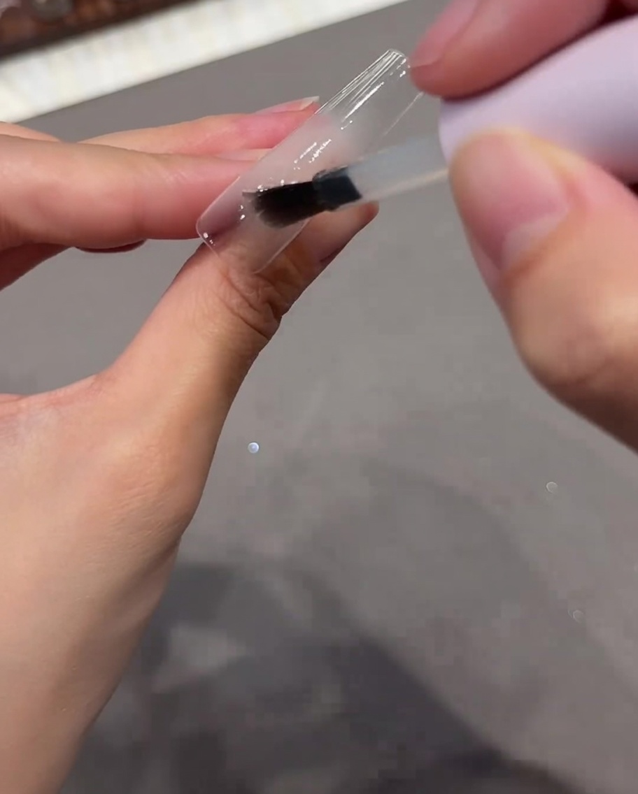 투명한 네일 팁에 베이스 코트 젤을 바르는 모습.