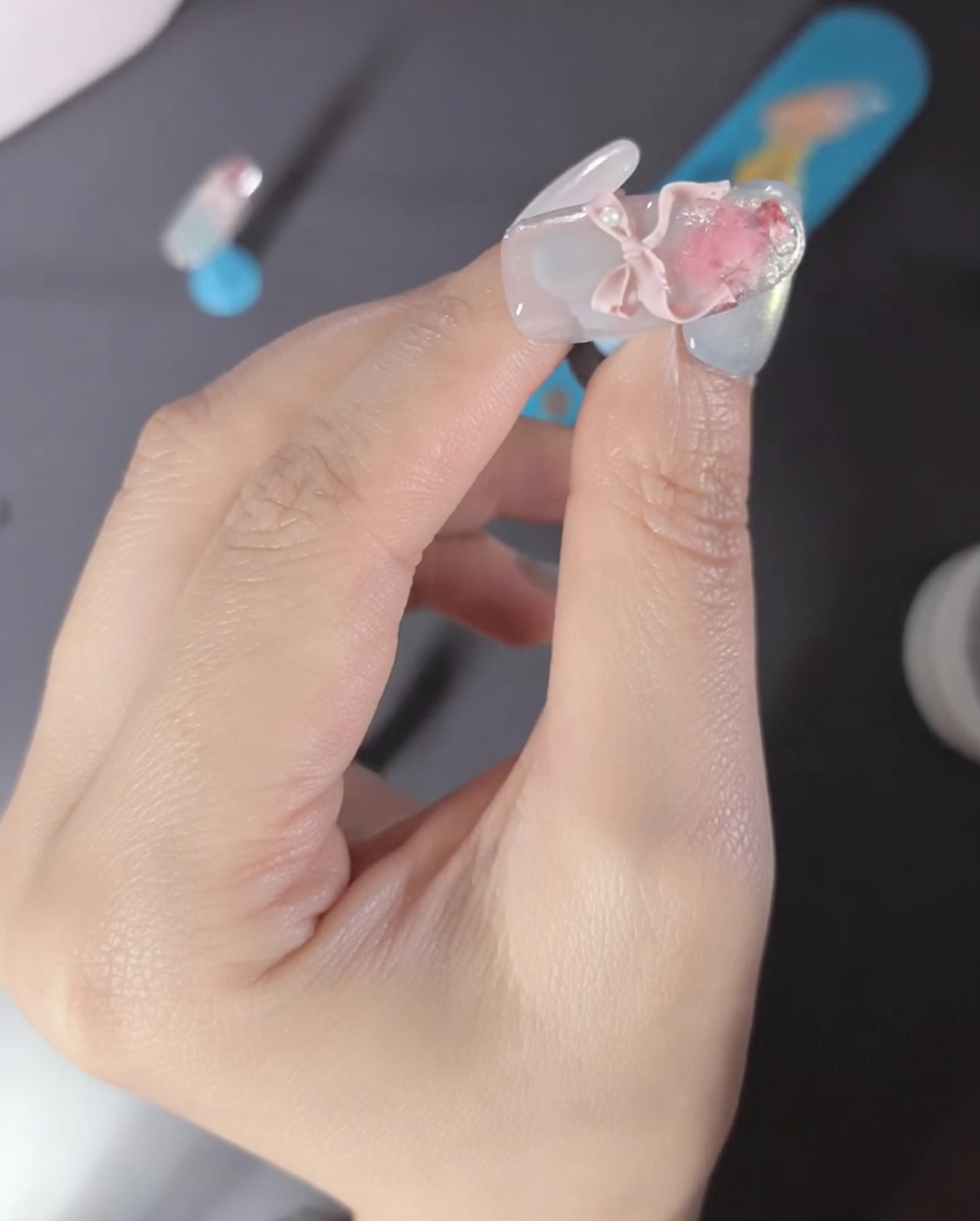 핑크색 3D 리본 파츠와 진주 장식이 달린 네일 근접 사진.