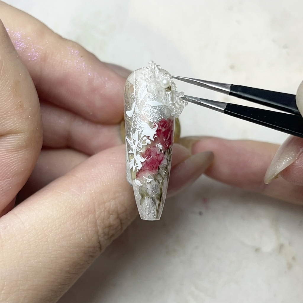 핀셋으로 작은 화이트 3D 꽃 참을 젤 글루 위에 정성스럽게 올리는 모습.