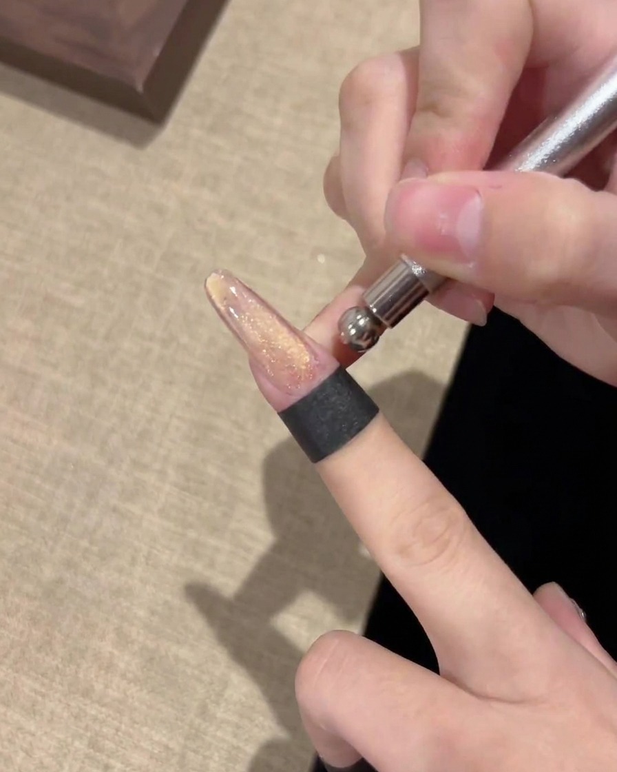금속 자석 도구를 손톱 수평으로 대고 위쪽으로 밀어 펄을 정교하게 다듬는 모습.