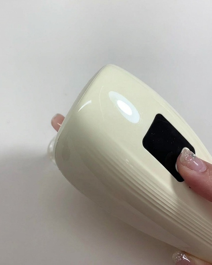 새로 칠한 누드 젤 네일을 큐어링하기 위해 미니 휴대용 UV/LED 램프를 들고 있는 손.