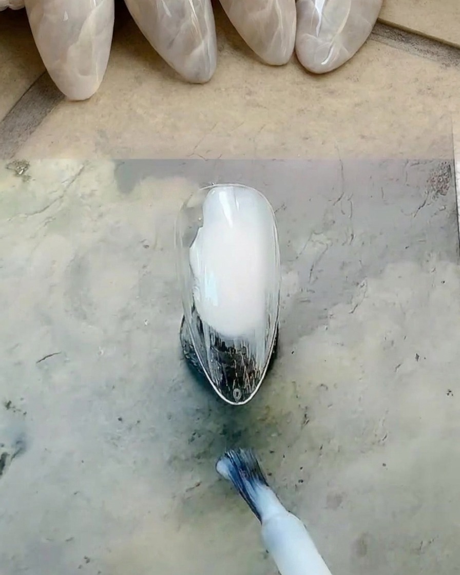 네일 브러시를 사용하여 손톱 전체에 밀키 화이트 젤 폴리시를 바르는 모습.