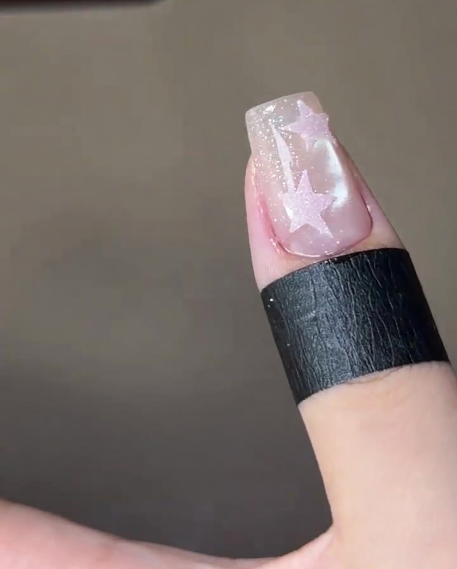 반짝이는 네일 위에 그려진 핑크색 별 위로 클리어 탑 코트를 바르는 클로즈업.