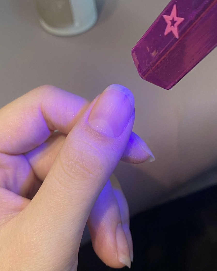 손톱을 보라색 휴대용 UV 램프 아래에 넣어 베이스 젤을 경화시키는 모습.