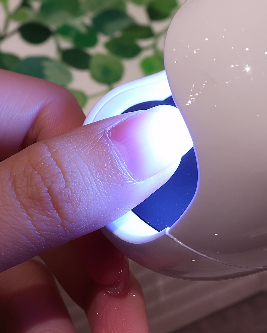 흰색 벨벳이 입혀진 손톱을 UV/LED 램프의 보라색 불빛 아래에 넣어 큐어링하는 모습.