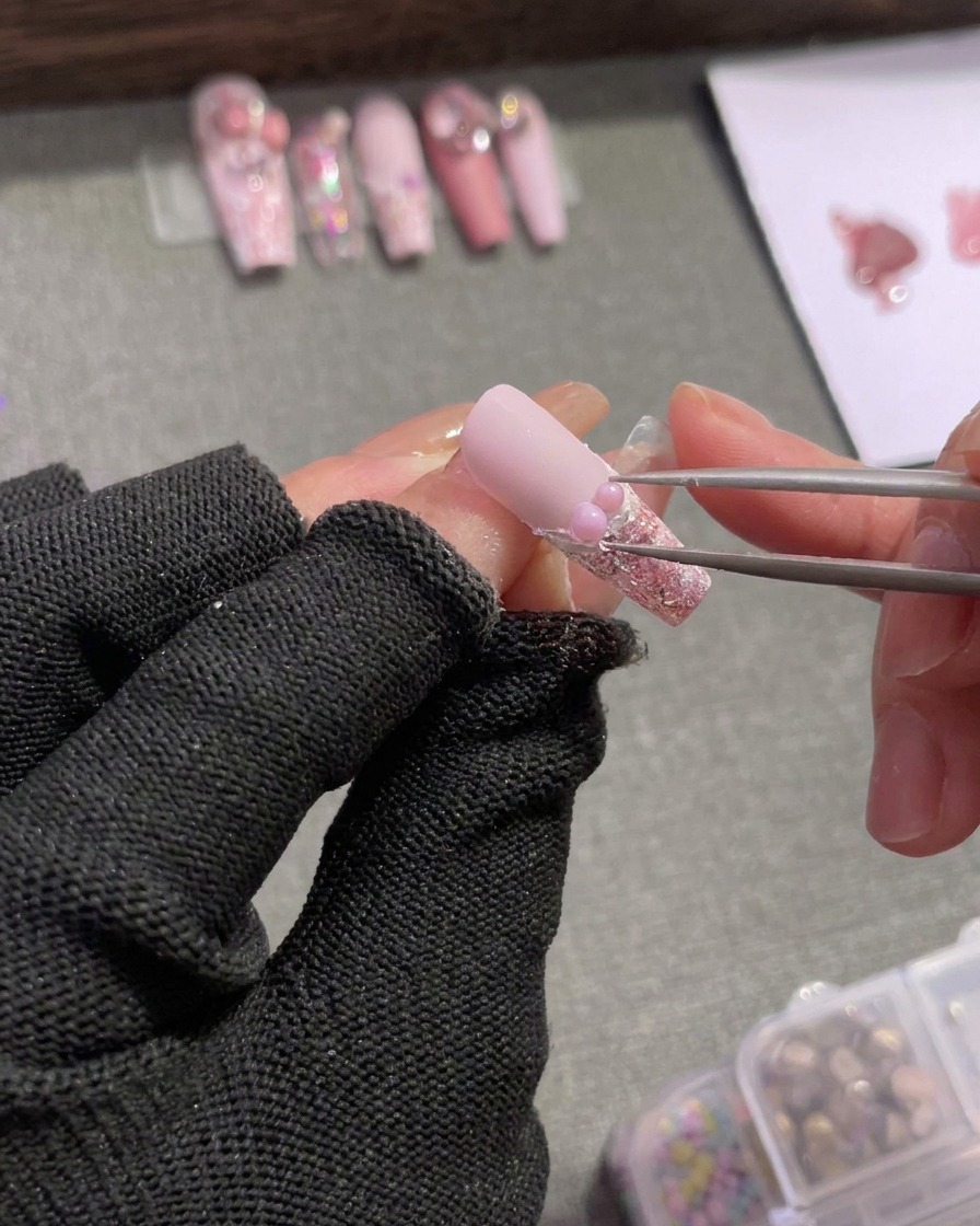 핀셋으로 실버 라인스톤과 작은 핑크 리본 참을 진주 옆에 배치하는 모습.