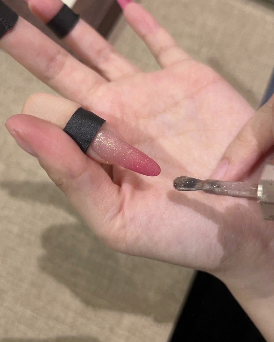마그네틱 쉬머 입자를 끌어당기기 위해 자석을 손톱과 평행하게 들고 있는 손.