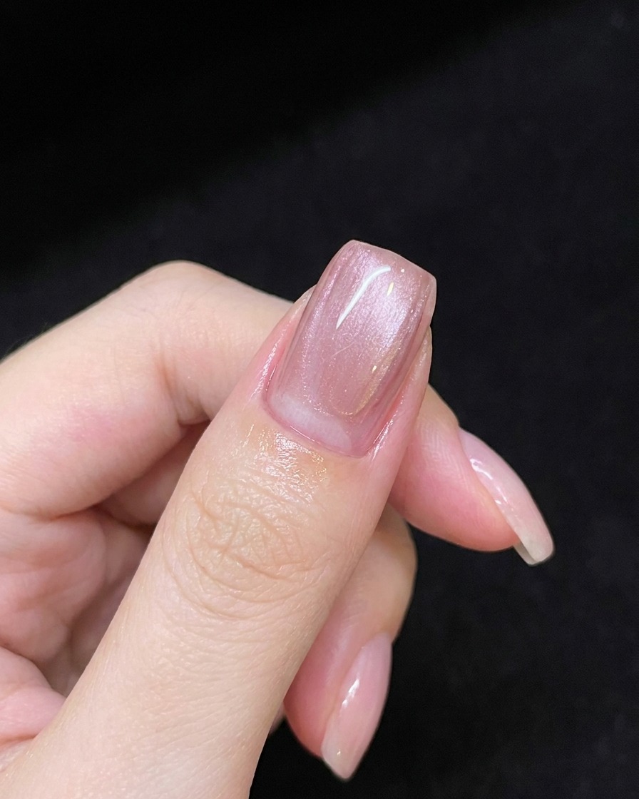 핑크 젤이 발린 손톱 위로 마그네틱 스틱을 띄워 대각선 형태의 시머 라인을 만드는 모습.
